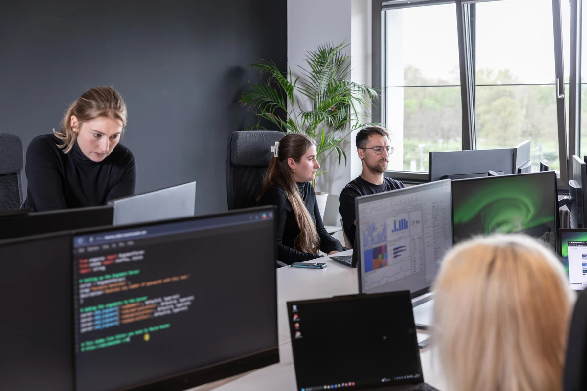 Mehrere IT-Spezialisten arbeiten nebeneinander an Monitoren an der Strukturierung von SQL Transformationen und Datenmodellen. Skalierbare Business Intelligence für datenbasierte Erfolge